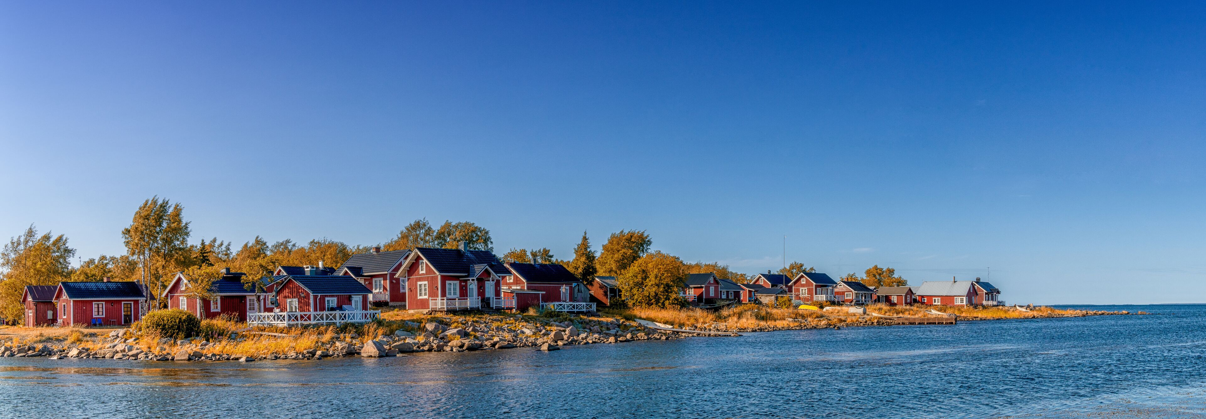 A row of red wooden houses by a calm body of water.