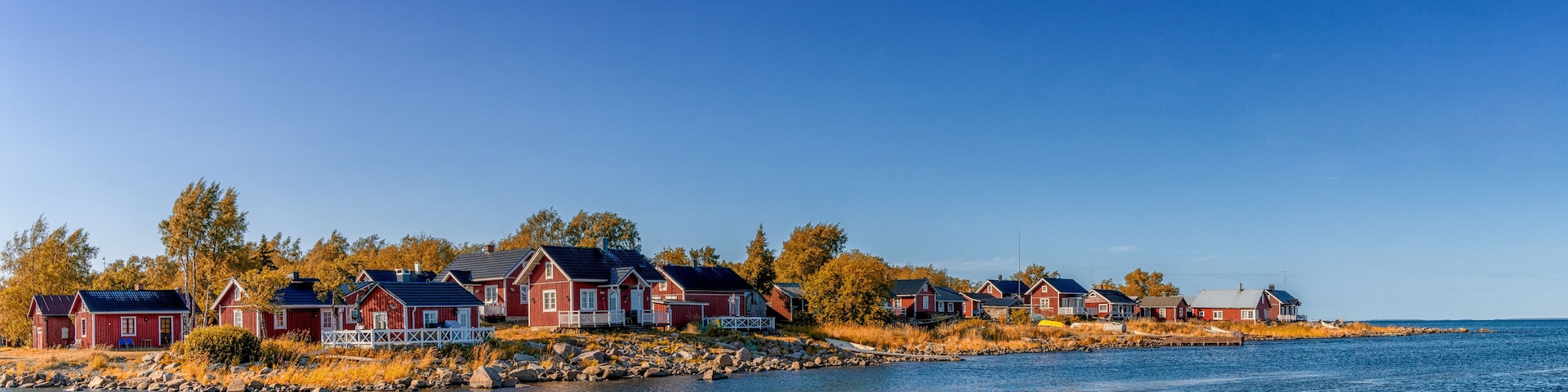A row of red wooden houses by a calm body of water.