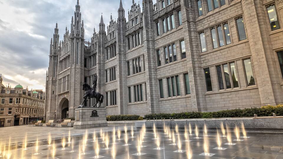 A grand building with a statue of a horse and rider, surrounded by a reflective water feature.