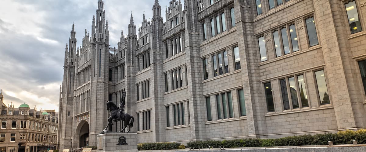 A grand building with a statue of a horse and rider, surrounded by a reflective water feature.