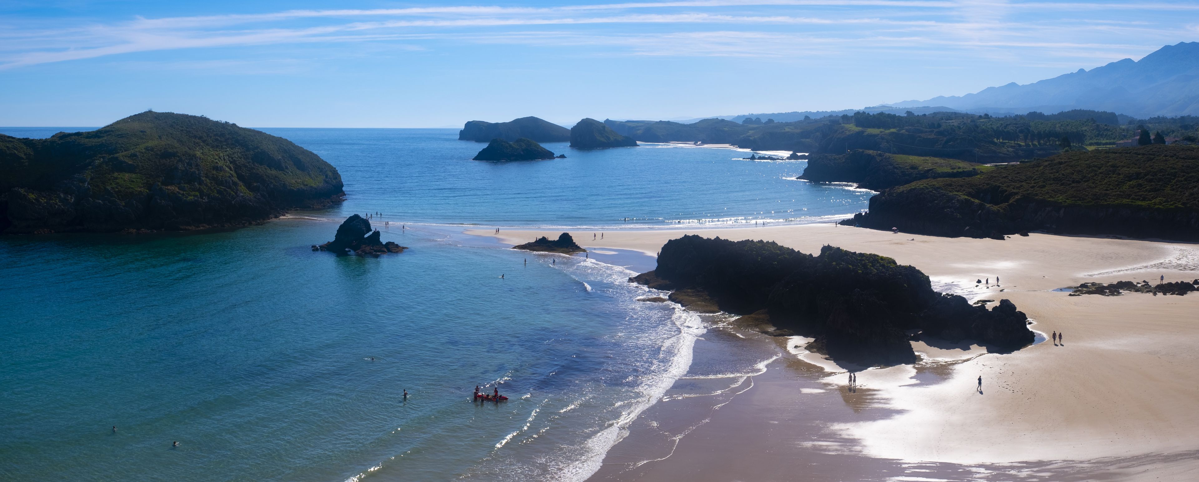 Un paisaje costero con afloramientos rocosos, agua azul cristalina y una playa de arena.
