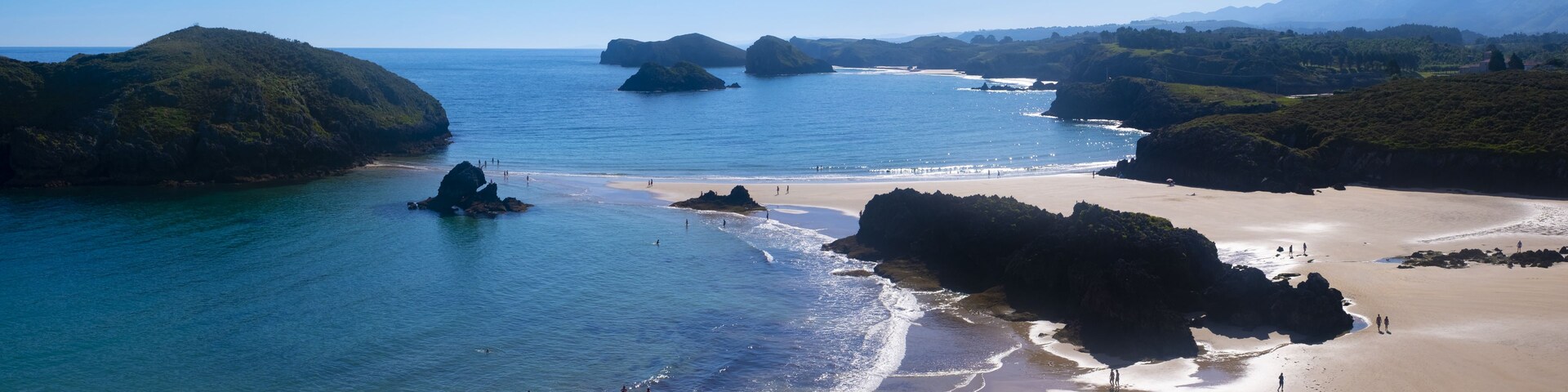 Un paisaje costero con afloramientos rocosos, agua azul cristalina y una playa de arena.