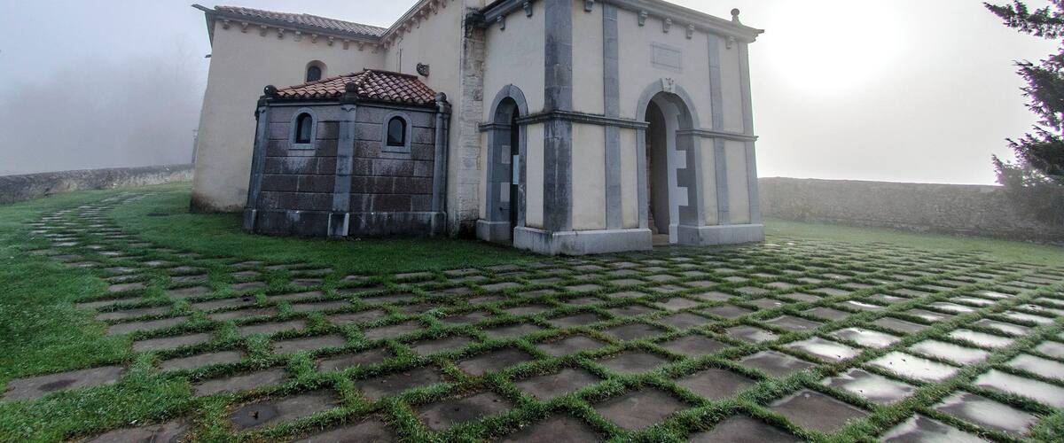 A church with a bell tower and a smaller adjacent building, surrounded by a paved area with grass growing between the paving stones.