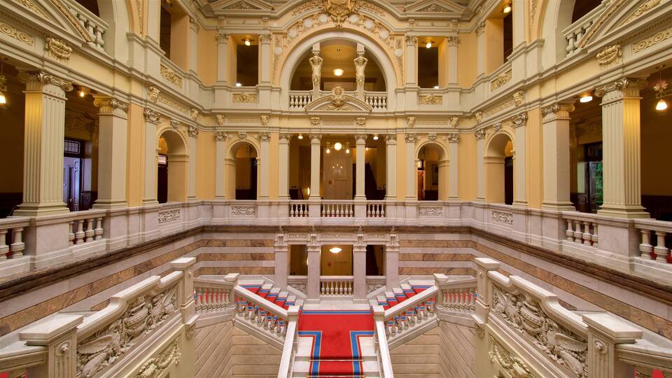 A grand, ornate building with multiple levels, large columns, and a central staircase with red carpeting.