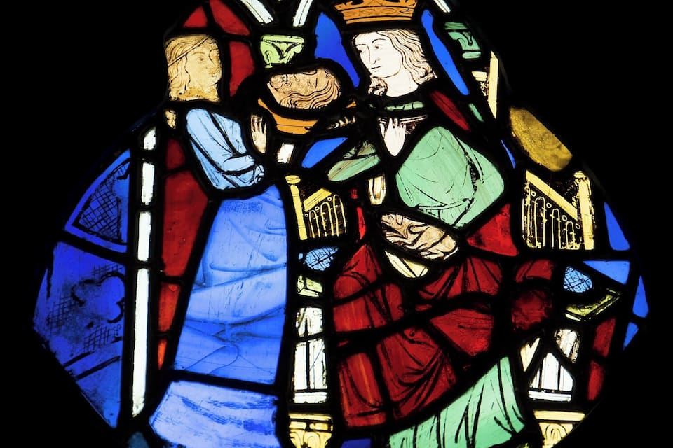 A stained glass window with figures in blue, red, and green robes.