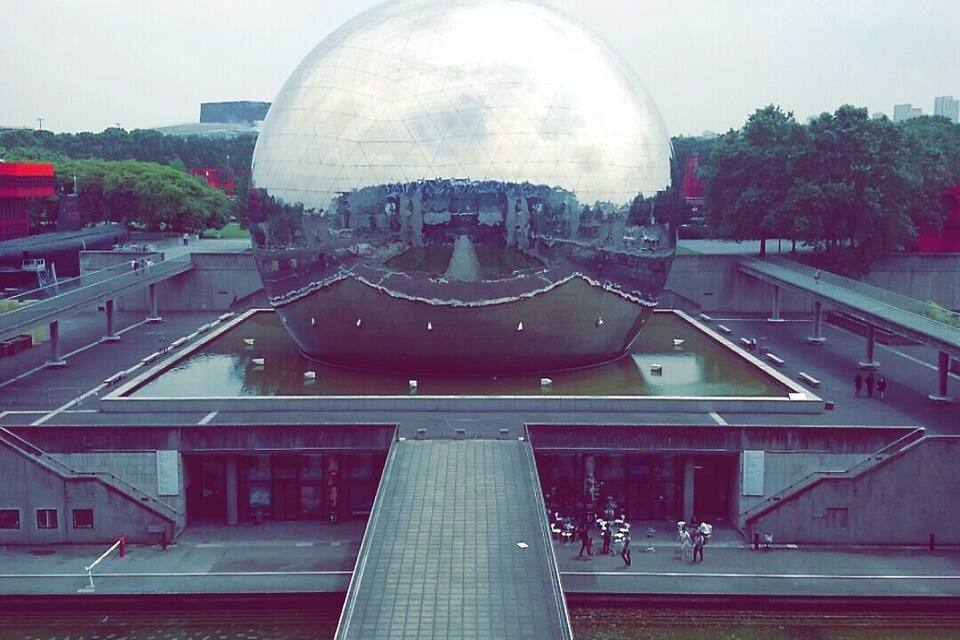 Een groot, bolvormig gebouw met een reflecterend oppervlak, omringd door een plein en een waterkanaal.