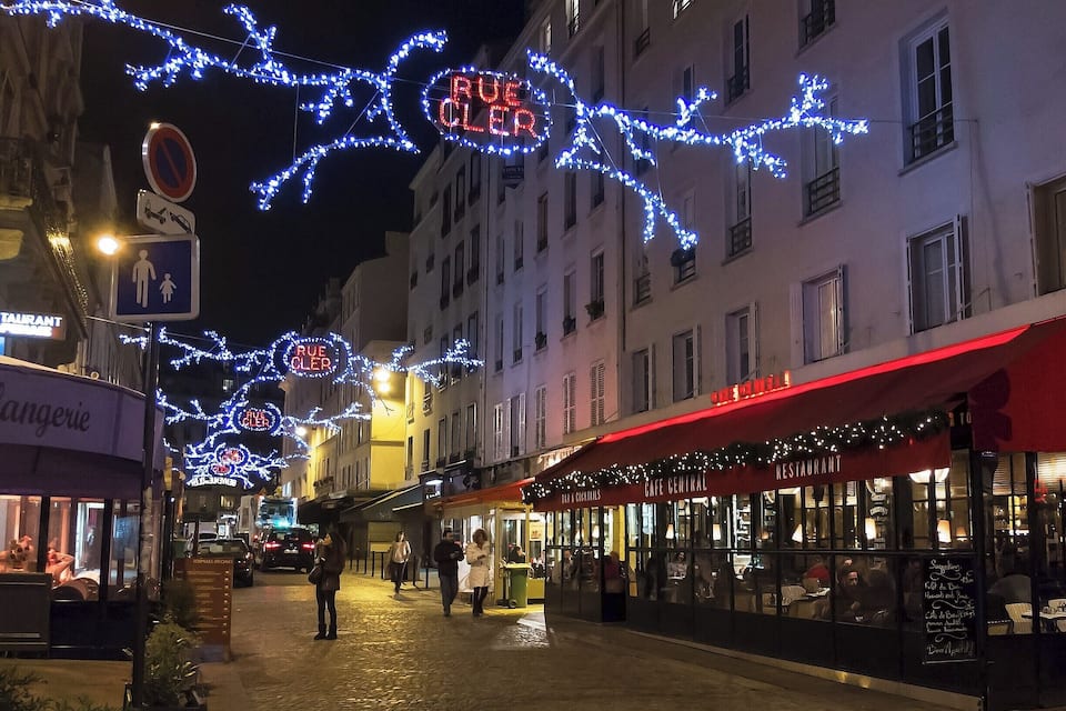 Eine Kopfsteinpflasterstraße bei Nacht mit beleuchteten Schildern und Geschäften, darunter ein Café und Restaurant.