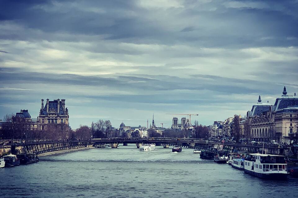 A river with boats, a bridge, and historic buildings under a cloudy sky.