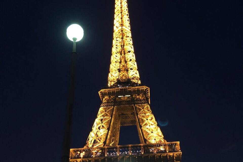 The Eiffel Tower at night with lights on, a statue of a horse, and a street lamp.