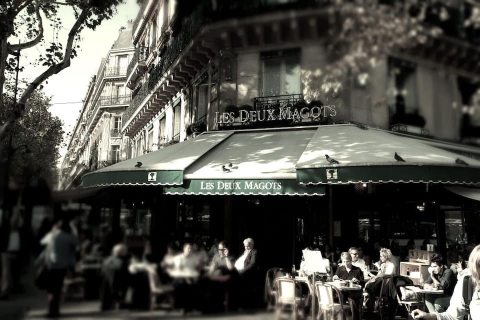 Un café al aire libre llamado 'Les Deux Magots', con gente cenando y pasando.