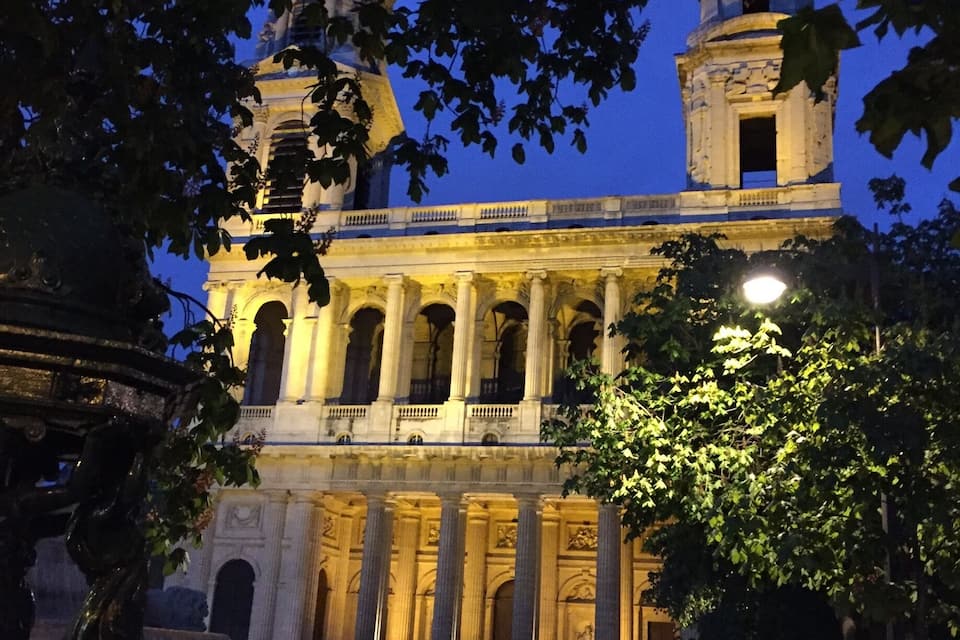 Un edificio histórico con columnas y una torre del reloj al anochecer.