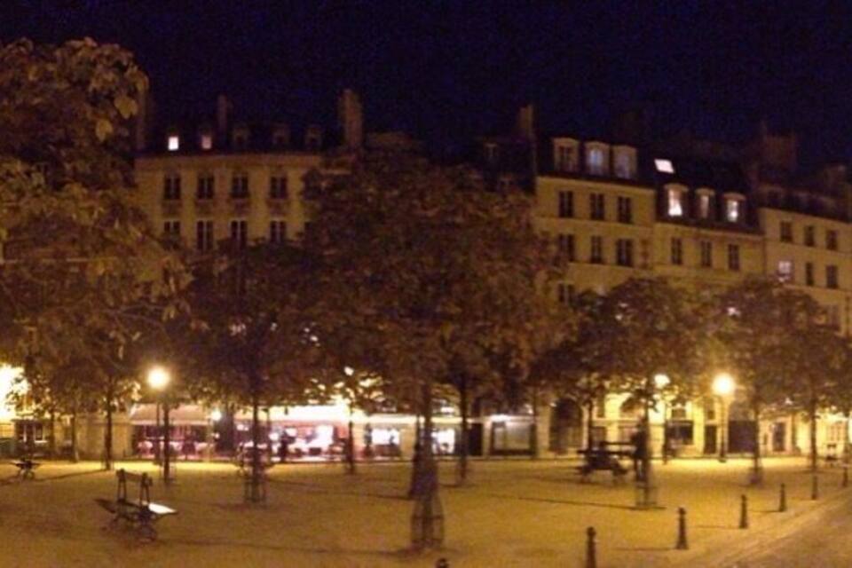 Una plaça urbana de nit amb arbres, bancs i edificis il·luminats.