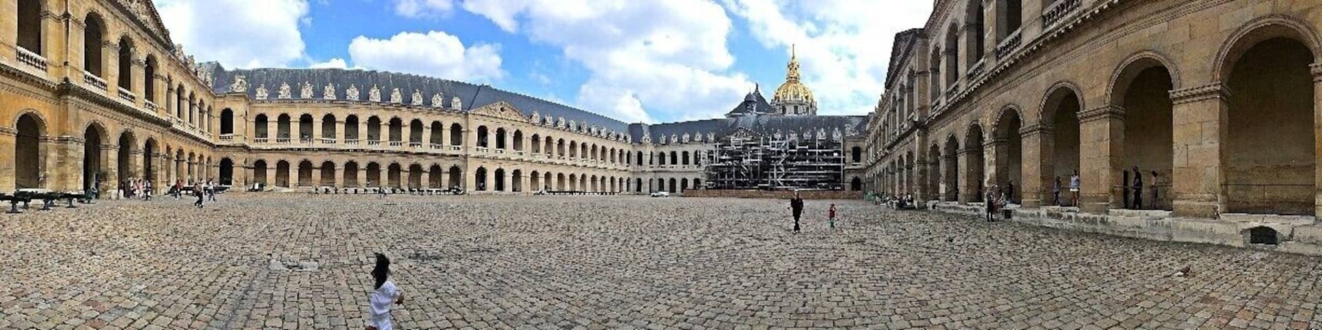 A large open courtyard with cobblestone paving, surrounded by classical architecture with arches and columns.