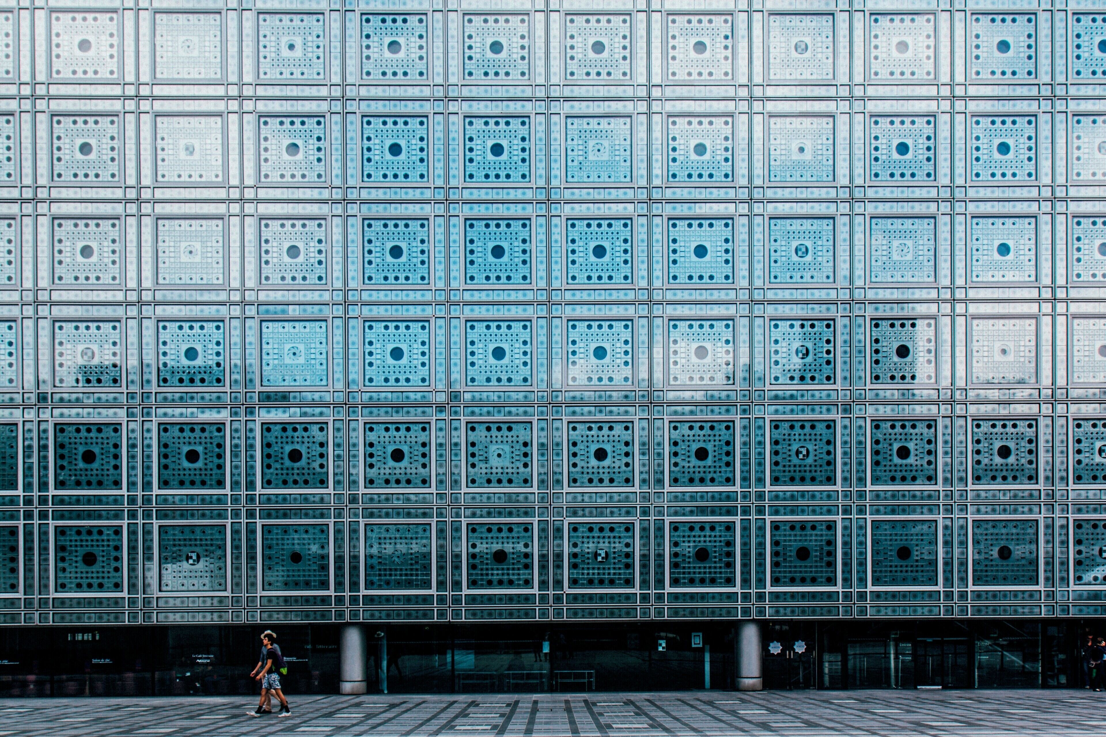 A modern building with a grid of square windows and a person walking in front.