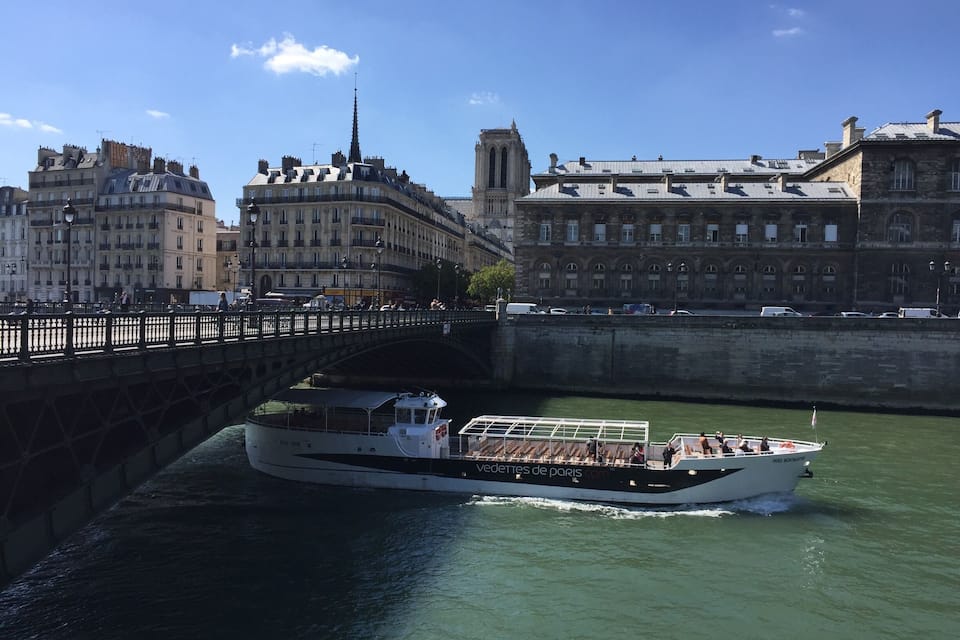 A boat on a river with a bridge and historic buildings in the background.