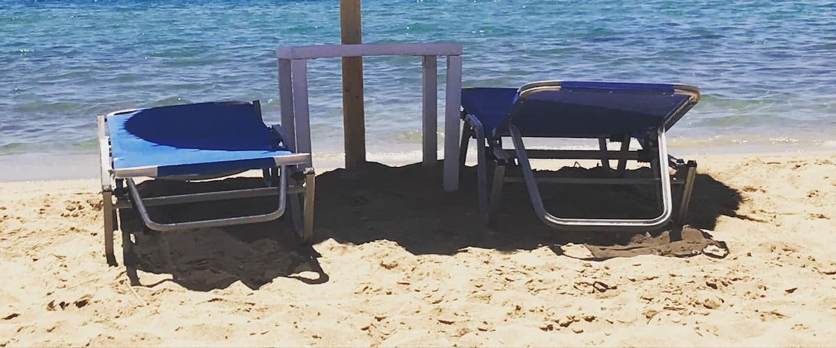 A beach with two blue lounge chairs and a straw umbrella.