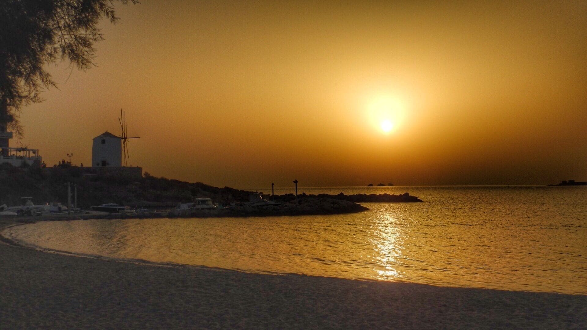 Atardecer sobre una zona costera con un molino de viento y un litoral rocoso.