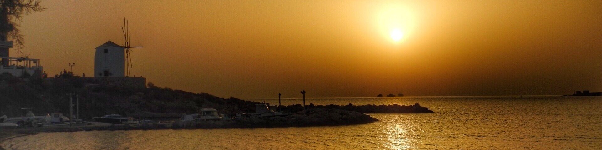 Atardecer sobre una zona costera con un molino de viento y un litoral rocoso.