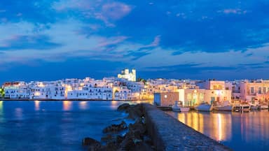 A coastal town at dusk with white buildings, a prominent church, and boats docked along the waterfront.