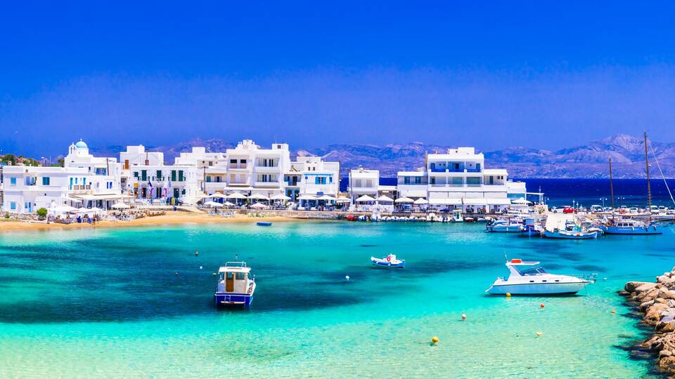 A coastal town with white buildings, a clear turquoise sea, and boats docked at the pier.