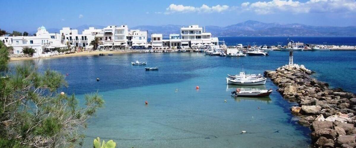 A coastal town with white buildings, a rocky breakwater, and boats in the water.