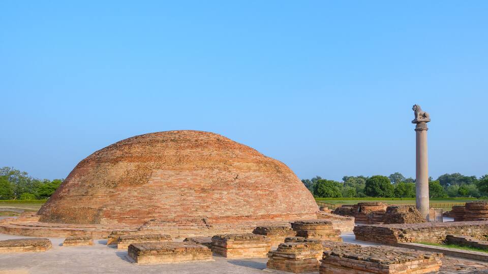 Ancient brick ruins with a large dome and a tall column with a statue.