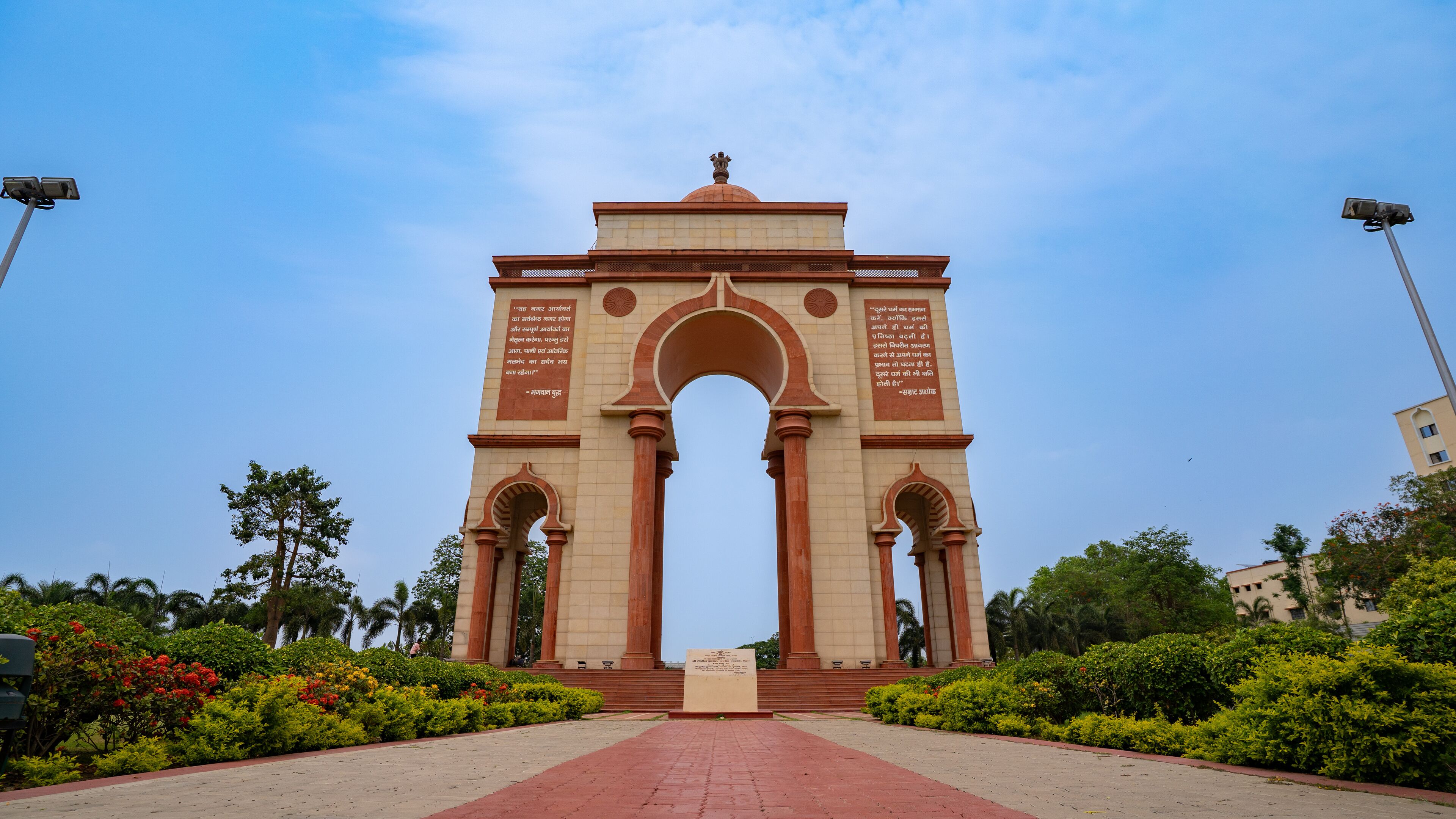 A large archway with inscriptions, surrounded by well-maintained greenery and palm trees.