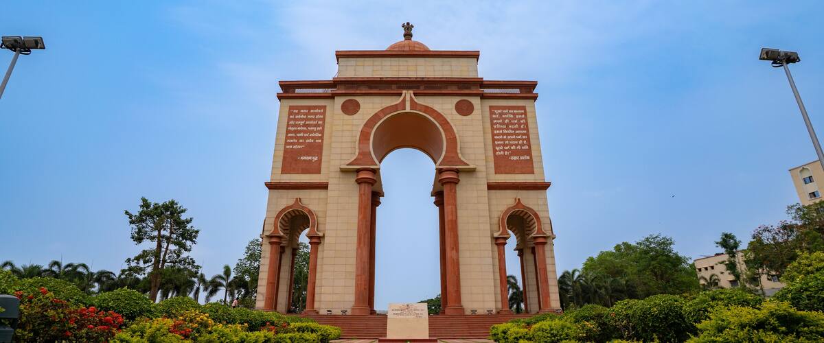 A large archway with inscriptions, surrounded by well-maintained greenery and palm trees.