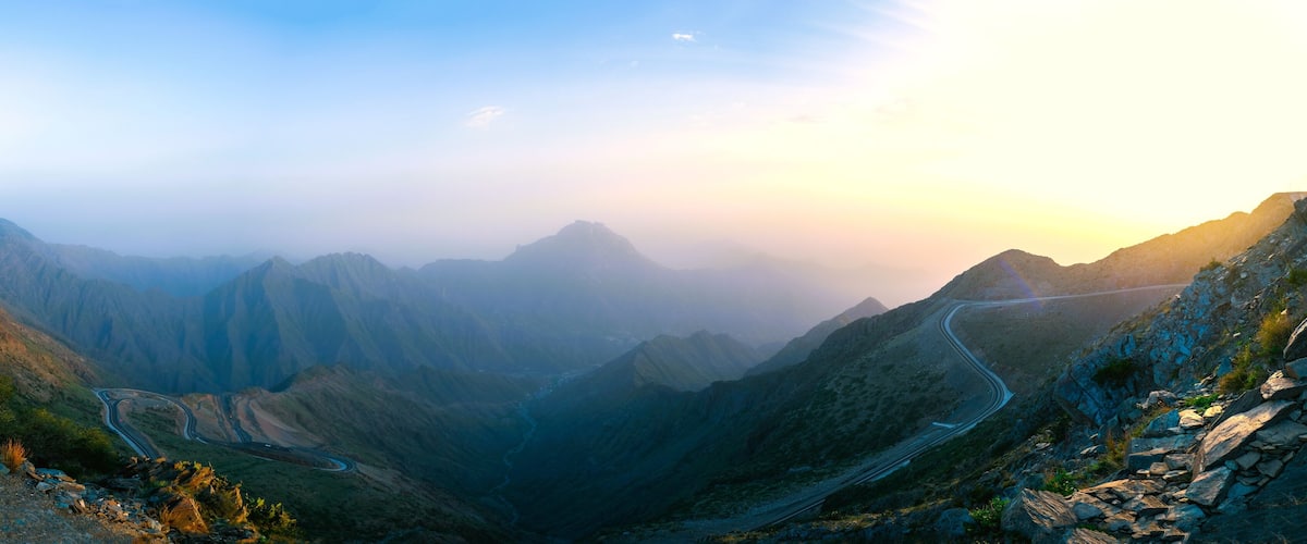 A winding mountain road through a canyon with steep cliffs and a clear sky.
