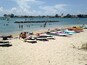 Une plage où l’on peut faire du kayak et du surf, où les gens se baignent et où des bateaux naviguent.