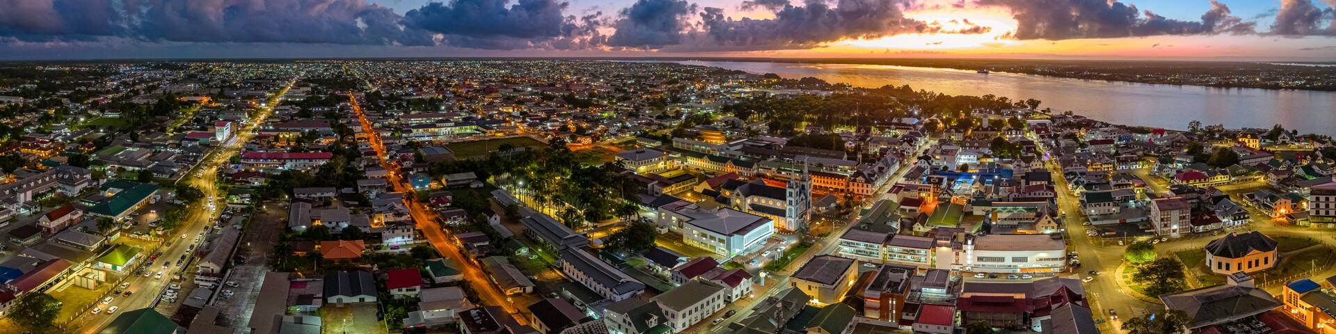 Aerial cityscape of Paramaribo, Suriname, featuring the historic Saint Peter and Paul Cathedral and surrounding colonial architecture bathed in beautiful sunrise light near the riverbank