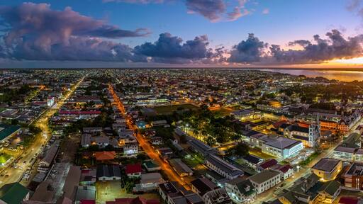 Aerial cityscape of Paramaribo, Suriname, featuring the historic Saint Peter and Paul Cathedral and surrounding colonial architecture bathed in beautiful sunrise light near the riverbank