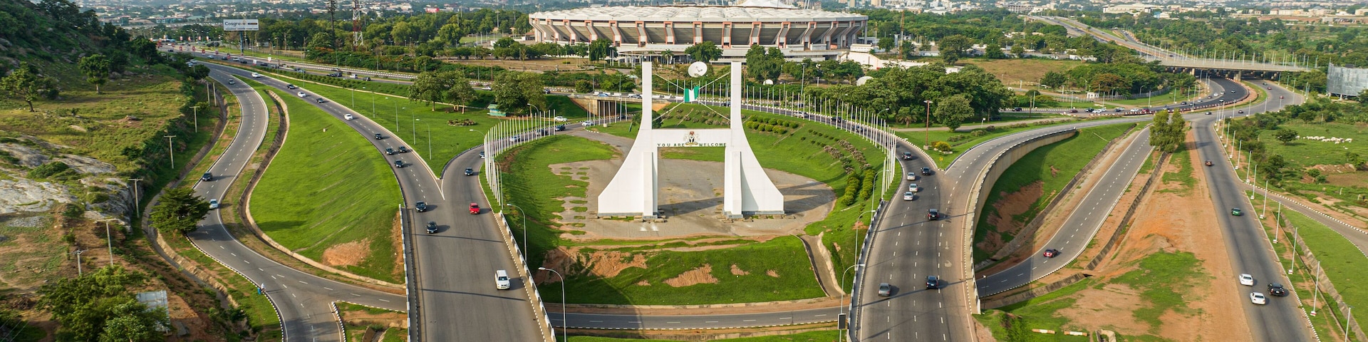 Um monumento branco grande com a inscrição "YOU ARE WELCOME" no centro de um canteiro, rodeado por áreas verdes e estradas.