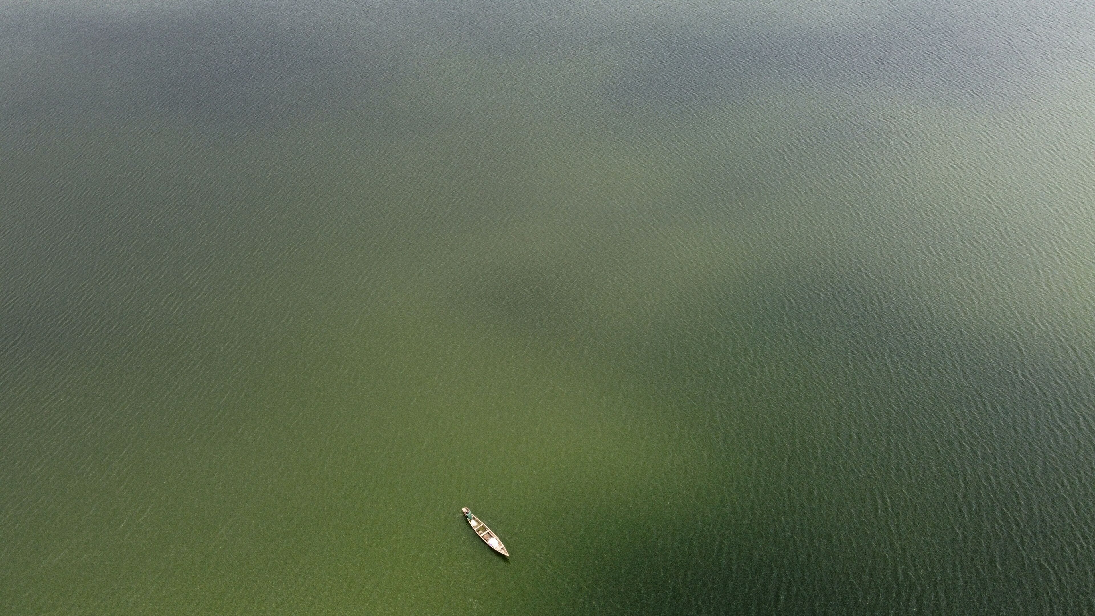 Aerial view of a lone canoe drifting on the tranquil, dark olive-green expanse of Jabi Lake, Abuja, Federal Capital Territory, Nigeria.