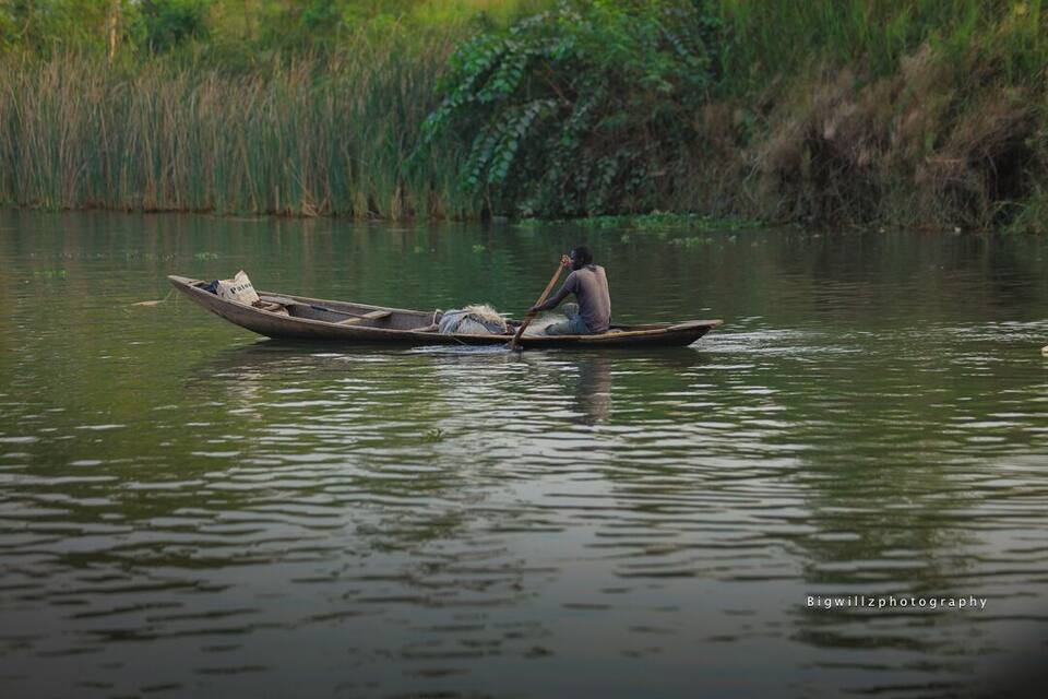 A person paddling a small boat on a calm river surrounded by lush greenery.