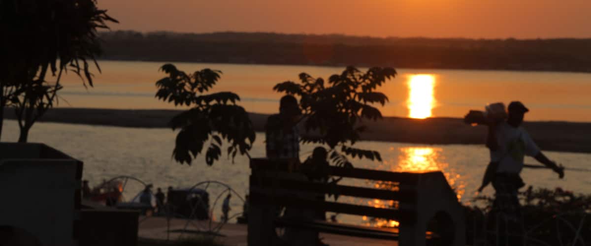 A sunset over a body of water with silhouettes of people and trees.