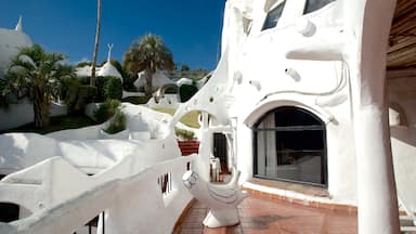 A white, sculptural building with unique architecture, palm trees, and a clear blue sky.