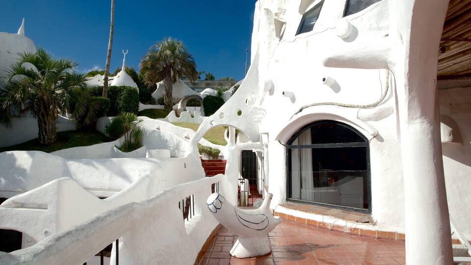 A white, sculptural building with unique architecture, palm trees, and a clear blue sky.