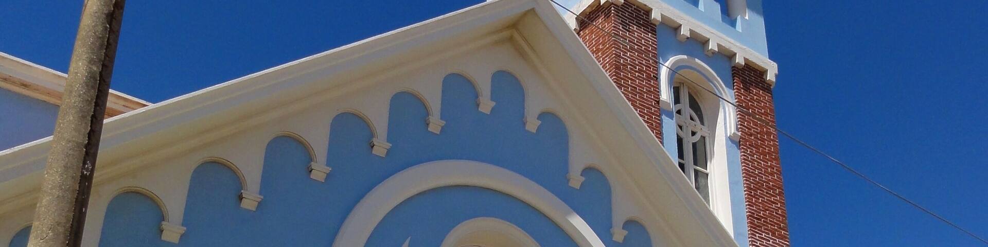 Una iglesia con fachada azul, arcos blancos y una torre con campanario.