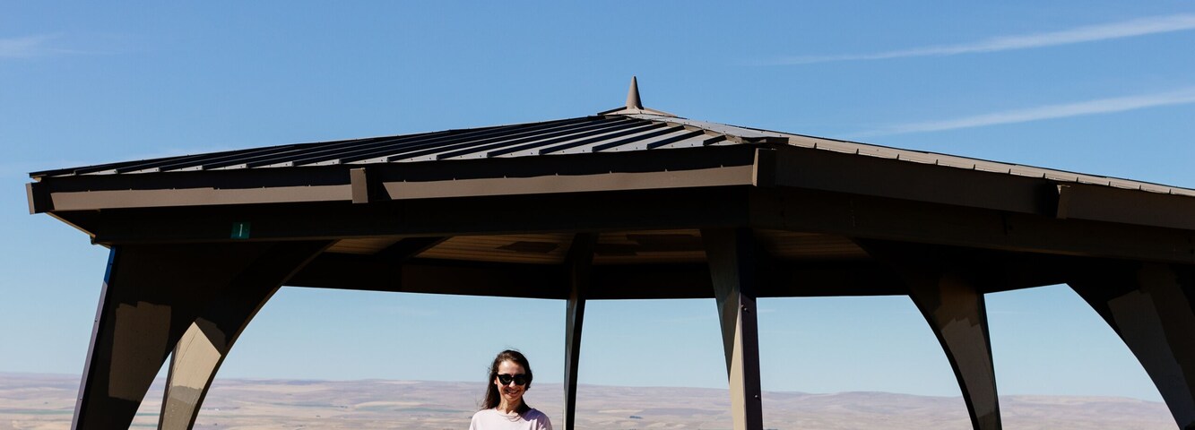 Una persona parada bajo un refugio con un cielo azul despejado al fondo.