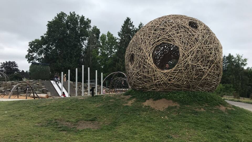 A large spherical structure made of intertwined branches in a park.