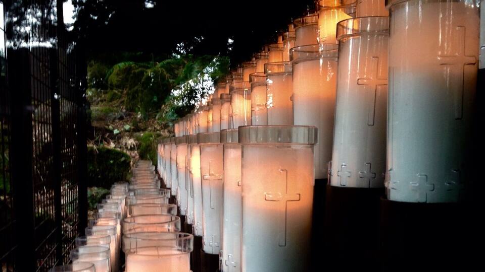 A row of lit candles in glass containers, arranged in a dimly lit outdoor setting.