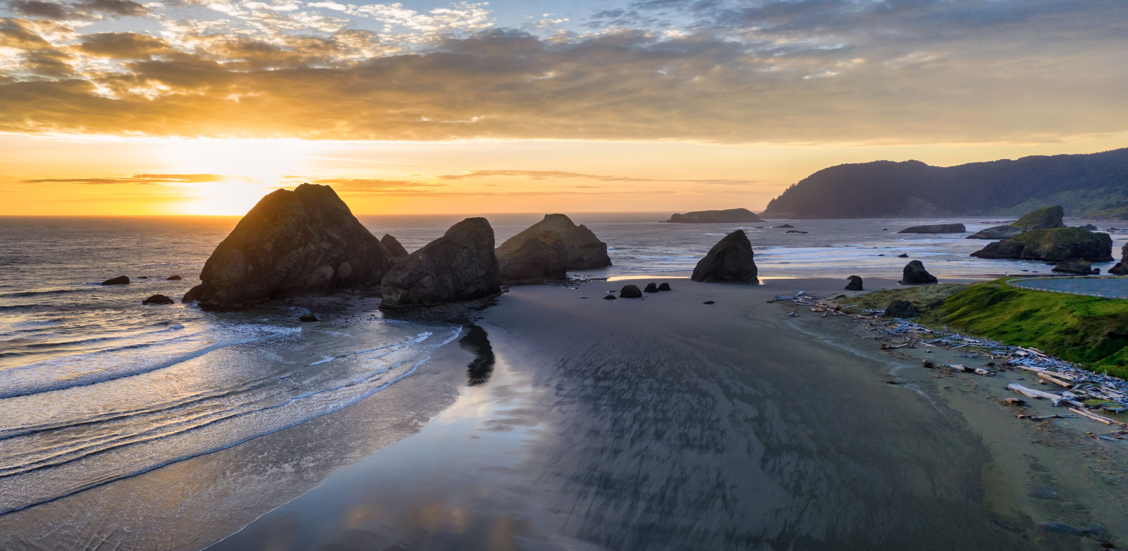 Un paisaje costero con grandes formaciones rocosas, una playa de arena y un atardecer.