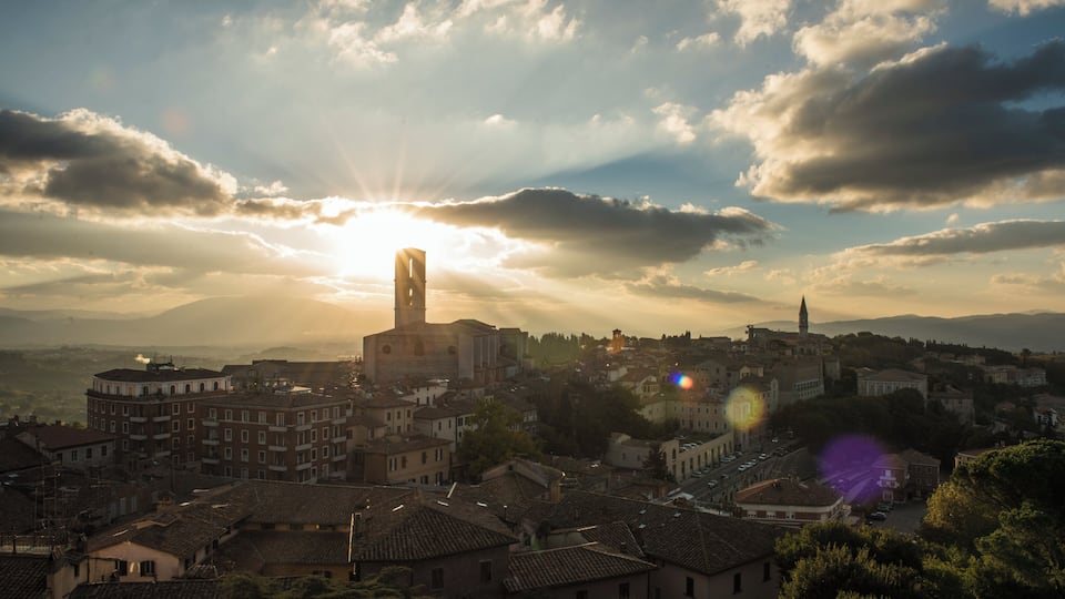 A town with a prominent church tower, surrounded by historic buildings and a clear sky with the sun setting.
