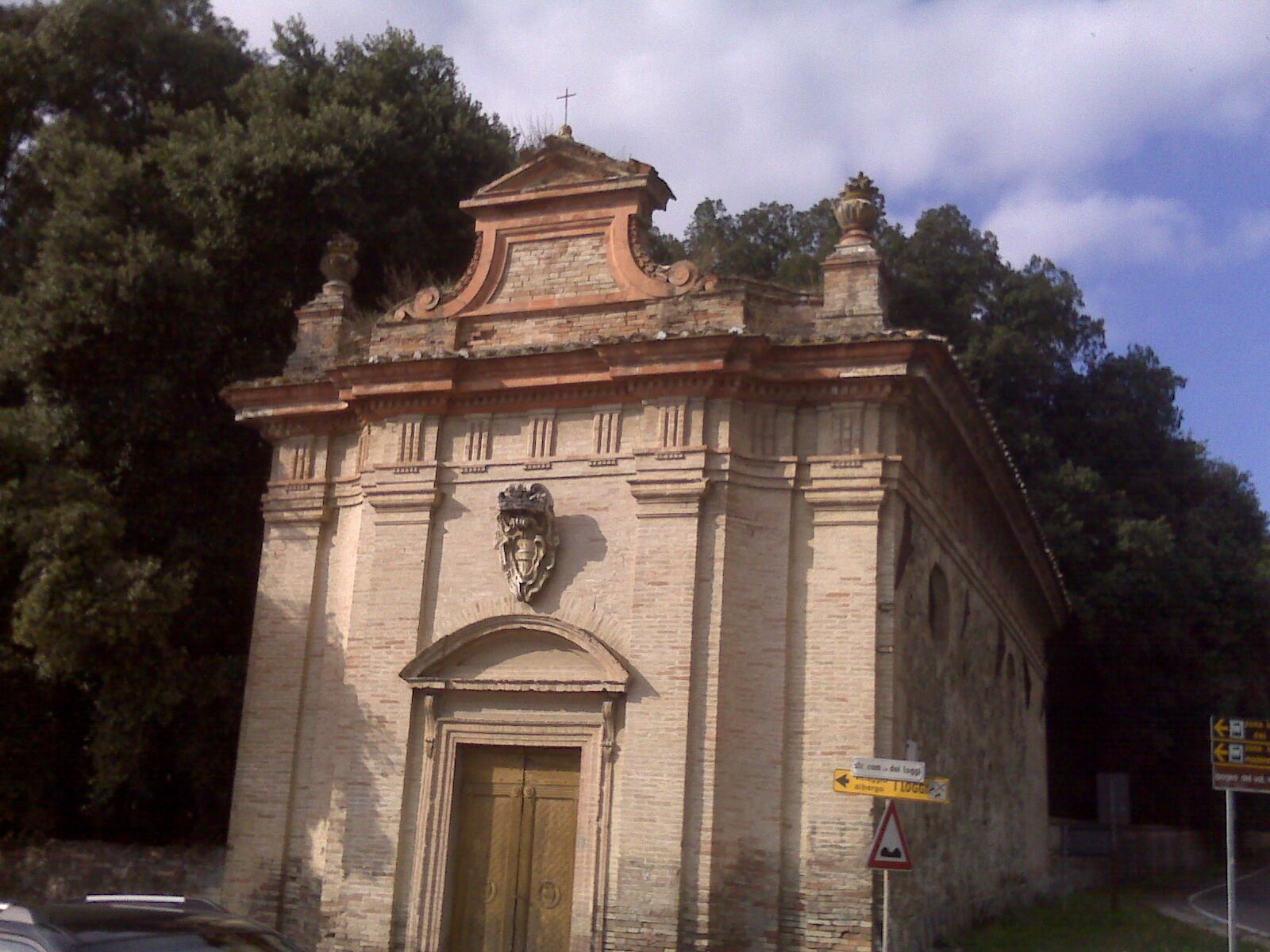 A small stone church with a cross on top, surrounded by trees.