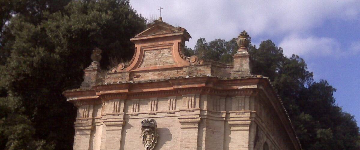 A small stone church with a cross on top, surrounded by trees.