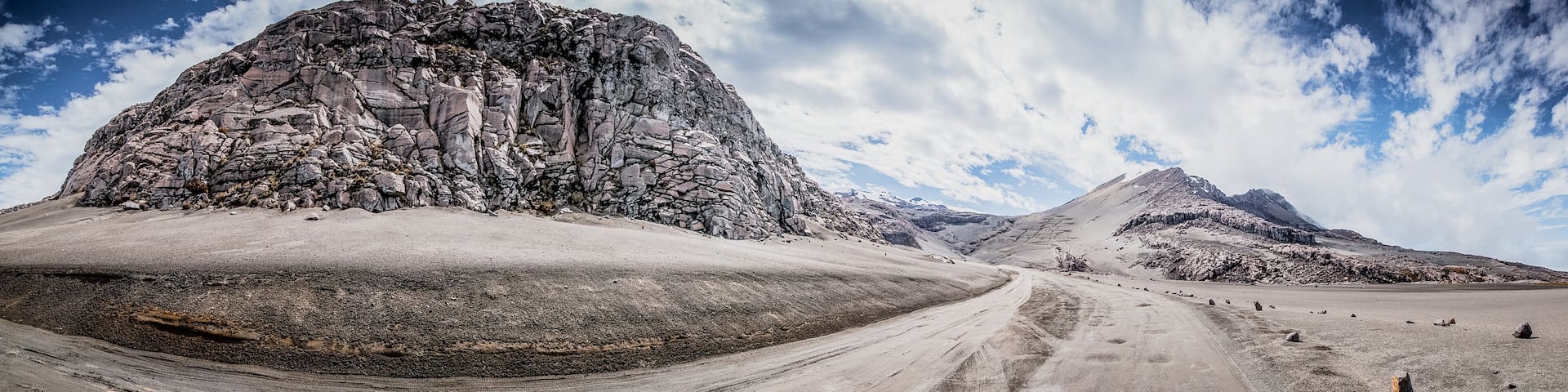 A rugged mountain landscape with a prominent rocky peak and a dirt road leading towards it.
