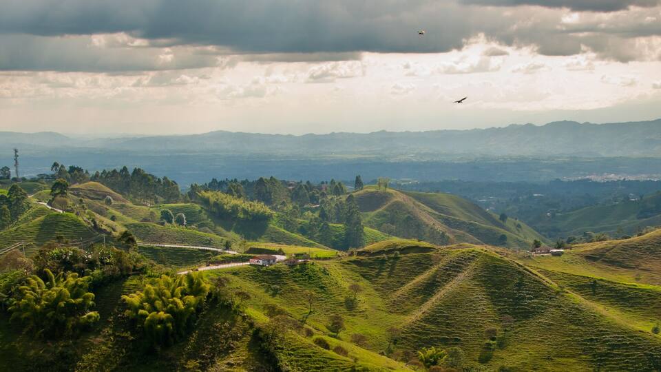 Rolling green hills with a winding road and a small building.