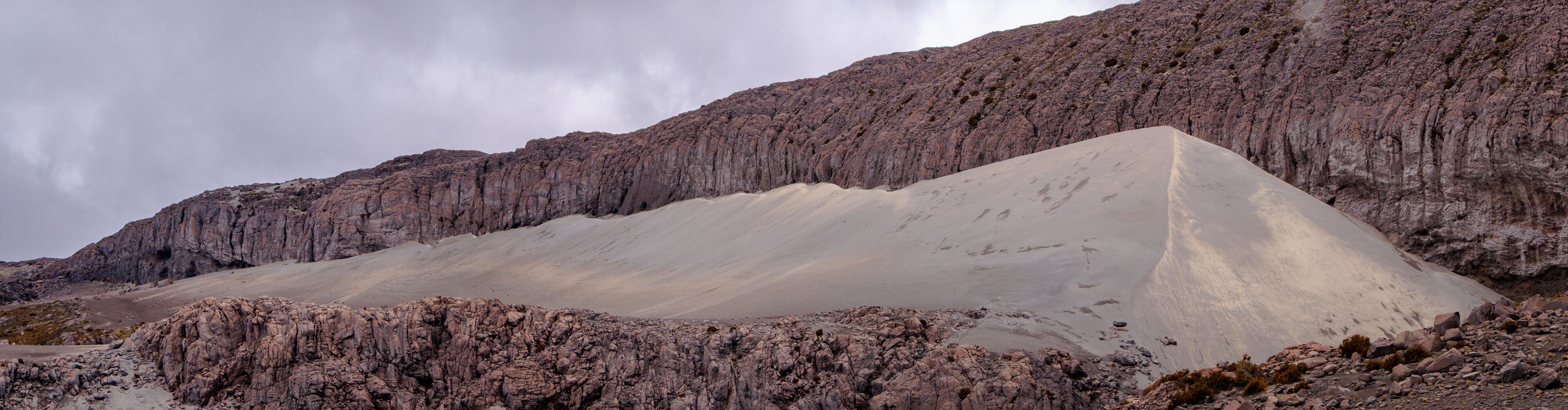 Panorámica de duna de ceniza volcánica blanca sobre pared de roca sedimentaria fracturada en el Parque Nacional Natural Los Nevados, Colombia. Contraste de texturas. Paisaje geológico, vasto y dramáti
