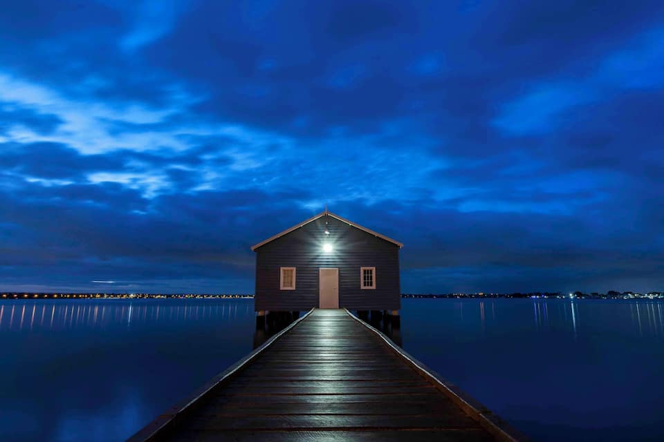 A wooden pier leading to a small house-like structure at night.